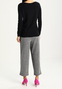 Pull noir côtelé, pantalon large gris chiné et talons hauts roses. Accent sur la texture du tricot et les contrastes de couleur.