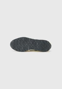 Black rubber shoe sole with a zigzag tread pattern and subtle branding; light-colored foam edge visible around the perimeter.