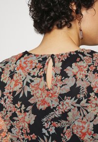 Blumenbluse mit schwarzem Grund und roten sowie grünen Mustern, runder Halsschnitt, Schlüsselrücken-Detail und schwarzem Knopfverschluss.