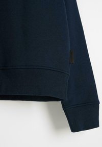 Granatowy sweter z miękkiej mieszanki bawełny, z ściągaczami na mankietach i u dołu, z małą metką marki z boku.