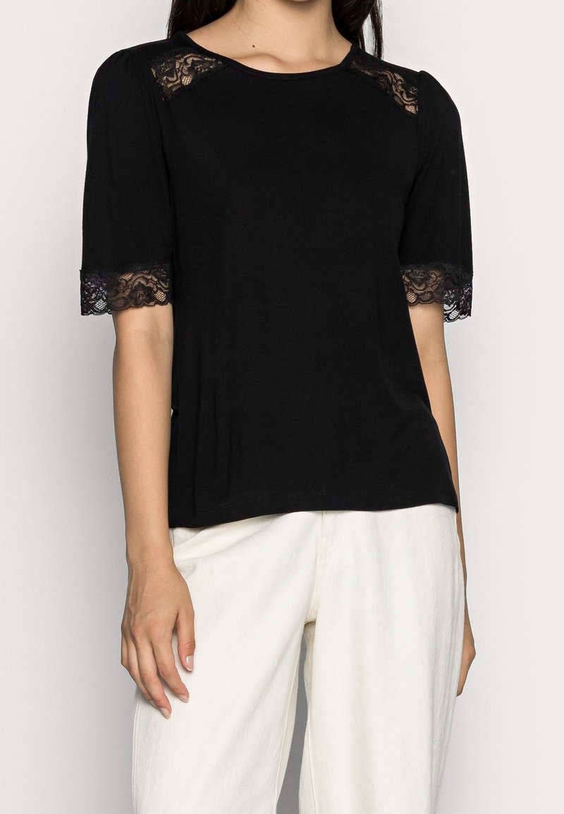 Haut noir à manches courtes avec dentelle. Doté d'un col rond et d'un ajustement décontracté, fabriqué en tissu doux. Accents aux épaules et aux manches.