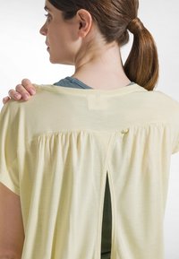 Lysegul, kortærmet top med løs pasform. Har et rynket design bagpå og en lille åbning bagpå, lavet af blødt stof.