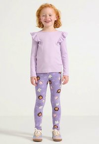 Hellviolettes Langarmshirt mit Rüschen an den Schultern, kombiniert mit violetten Leggings mit niedlichen Tier- und Figurenmotiven. Leichte Schuhe.