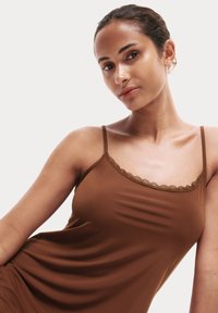 Camisola marrone con bordo in pizzo, dotata di spalline sottili e regolabili e una texture di tessuto liscia, progettata per una silhouette aderente.