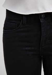 Jeans de mezclilla negra con una textura suave, que cuentan con un bolsillo frontal, cierre de botón y un diseño ajustado en la cintura y las caderas.