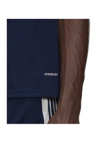 Maglietta sportiva blu navy con una texture liscia, con l'etichetta "AEROREADY" in bianco sul bordo inferiore. Vista parziale di un braccio muscoloso.