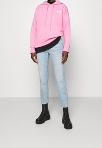 Felpa rosa con cappuccio e tasca frontale, sovrapposta a una maglietta nera, abbinata a jeans dritti blu chiaro e stivali neri con plateau.