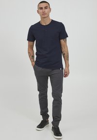 Marineblå kortermet henley t-skjorte med fire knapper, kombinert med grå bukser og svarte sneakers, med en glatt tekstur og en tettsittende design.