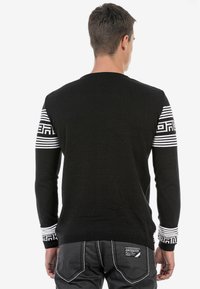 Schwarzer Pullover mit langen Ärmeln und weißen Musterakzenten an den Bündchen. Hergestellt aus einem strukturierten Stoff mit Rundhalsausschnitt.