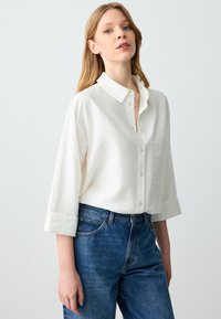 Witte button-up shirt van textuurstof, met een puntige kraag en opgerolde manchetten, gecombineerd met hoog opgesneden blauwe denim jeans.