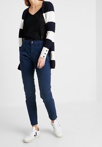 Námořnické modré kalhoty s přiléhavým střihm, v kombinaci s černým topem s výstřihem do V a pruhovaným otevřeným cardiganem. Outfit doplňují bílé tenisky.