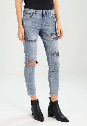 Jasnoniebieskie, podarte skinny jeansy z czarnymi cekinowymi naszywkami, noszone z czarnymi botkami i włożonym do środka czarnym topem.