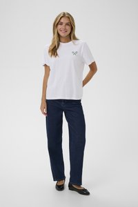 Weißes Baumwoll-T-Shirt mit einem grünen Tennisschläger-Design, kombiniert mit dunkelblauen geraden Jeans und schwarzen flachen Schuhen.