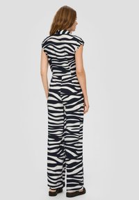 Combinaison à rayures zèbre noir et blanc avec des manches courtes, une taille ajustée, des pantalons évasés et un col. Le tissu semble léger et texturé.