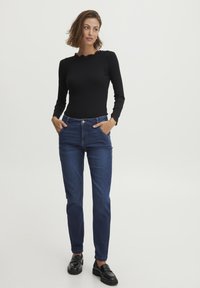 Černý top s dlouhými rukávy a vlnitým výstřihem, spárovaný s tmavomodrými slim fit džíny a černými koženými mokasínami. Jednoduchý a klasický design.