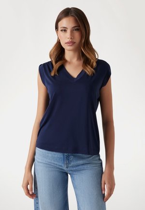 Top senza maniche di colore blu navy con scollatura a V, texture morbida e vestibilità comoda, abbinato a jeans di denim blu chiaro.