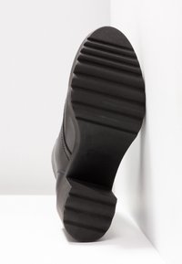 Black rubber sole of a boot featuring a textured grip with prominent ridges and a slight heel, complemented by a smooth upper edge.