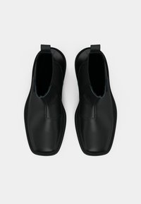 Mustat nahka nilkkurit, joissa on elastiset sivut, neliönmuotoiset varpaat ja minimaaliset ommeltut yksityiskohdat. Litteät pohjat, joissa on sileä pinta.