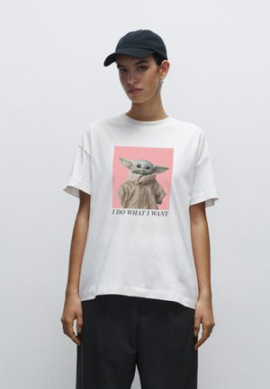 T-shirt blanc surdimensionné avec un graphique d'un personnage fictif sur un fond rose, accompagné du texte "JE FAIS CE QUE JE VEUX" en dessous.