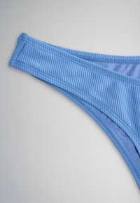 Kék bordázott anyagból készült bikini alsó dupla varrással, világosszürke háttéren.