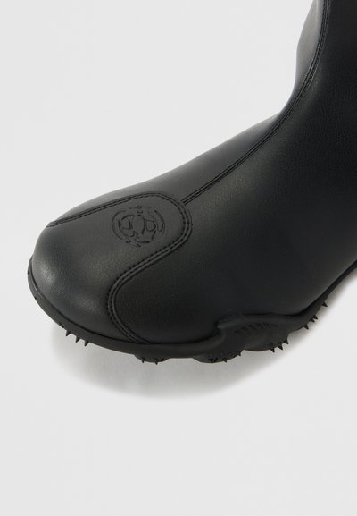 Black rubber boot with a smooth finish, rounded toe, and textured sole featuring small spikes. Logo embossed on the side.