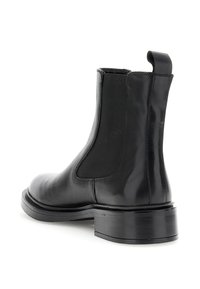 Botín Chelsea de cuero negro con panel lateral elástico, lengüeta en la parte posterior y tacón bajo apilado, en ángulo para mostrar el lado exterior y el tacón.