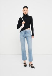 Top a collozzo nero a coste, jeans azzurri a gamba dritta e décolleté neri con punta affusolata e dettagli a fascia. Inoltre, una piccola borsa rosa.