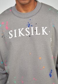 Sudadera gris con el logo "SIKSILK" en blanco, adornada con patrones de salpicaduras coloridas en rosa, verde, azul, naranja y negro.