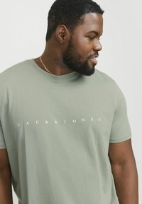 Lys grøn bomulds T-shirt med rund hals, der har "JACK & JONES" trykt i hvidt over brystet. Korte ærmer, afslappet pasform.