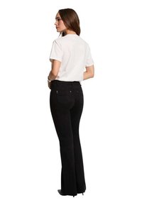 Jeans de mezclilla negros acampanados, con una cintura alta y sutiles bolsillos traseros, combinados con una camiseta blanca lisa.