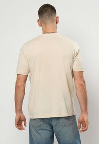 Béžové bavlnené tričko s krátkymi rukávmi, okrúhlym výstrihom, jednoduchým dizajnom a rovnakým strihom, nosené s svetlomodrými denimovými džínami.