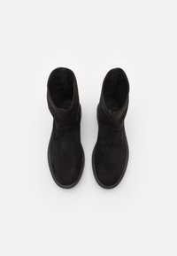 Bottes cheville en daim noir avec une texture lisse, un bout rond et une semelle texturée. Présentent un design simple sans aucune quincaillerie visible.