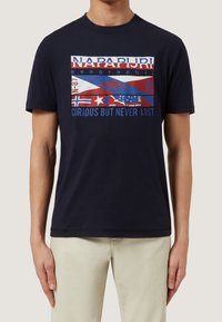 Mörkblå t-shirt med kort ärm som har ett flerfärgat grafiskt tryck med flaggor och text. Tillverkad av bomull; mjukt material. Avslappnad passform.