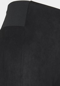 Tessuto scamosciato nero con una superficie texturizzata; presenta una cintura elastica liscia nella parte superiore, evidenziando un design aderente.