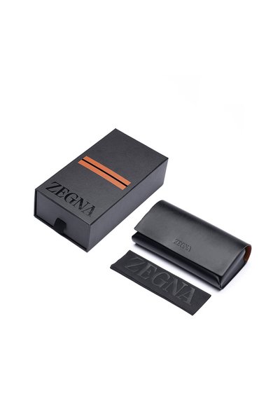 Czarna skórzana etui na okulary z wytłoczonym logo "ZEGNA", w zestawie z dopasowaną czarną papierową osłonką oraz prostokątnym pudełkiem w brązowe paski.