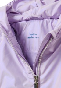 Lila ritsjack met een gladde, glanzende textuur. Heeft een gevoerd interieur en een zilveren rits. Het label geeft de maat aan voor 9-12 maanden.