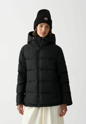 Zwarte pufferjack met een luipaardpatroon, rits sluiting, zijzakken en een afneembare capuchon. Gecombineerd met een geribbelde zwarte beanie.
