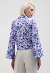 Veste à imprimé floral avec des manches longues et larges, fabriquée en tissu léger dans des teintes de violet et de bleu. Design court avec un col.