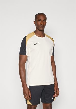 Nike športová košeľa v krémovej farbe s zlatými a čiernymi akcentmi. Má krátke rukávy, okrúhly výstrih a logo na ľavej hrudi.