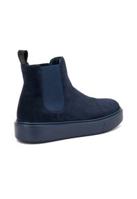 Botín Chelsea de ante azul marino con paneles laterales elásticos, tirador y suela de goma gruesa, que presenta una textura suave y un diseño de puntera redondeada.