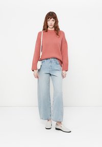 Rustfarget strikket genser med brede ermer, kombinert med lyseblå høytlivsjeans. Modellen har på seg beige slip-ons.