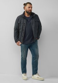 Marynarka w kolorze granatowym z kieszeniami z przodu, noszona na ciemnoniebieskiej koszuli. Ubrana w jasnoniebieskie dżinsy i trampki w kolorze kremowym z brązowymi akcentami. Casualowy styl.