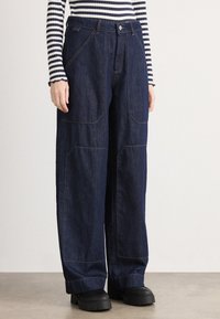 Vide ben, mørkeblå denimbukser med frontlommer og kontrasterende s�ømmer. Glatt tekstur og strukturert design. Kombinert med svarte plattformsko.