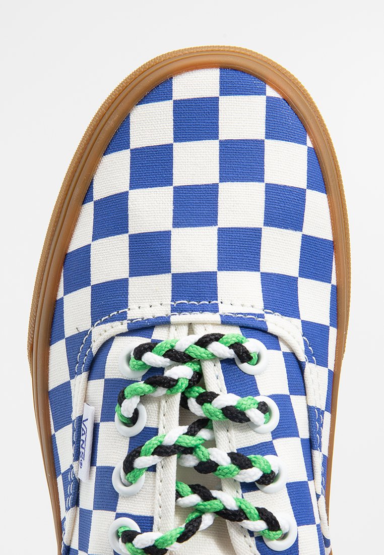 Baskets en toile à carreaux bleus et blancs avec des lacets à motifs verts, noirs et blancs, semelle en caoutchouc et étiquette de logo sur le côté.