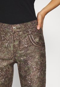 Bruine en groene jeans met paisley-patroon en een gestructureerde stof, voorzien van een knoopsluiting en decoratieve zijstiksels op de zakken.