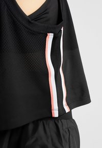 Lähikuva mustasta urheilunettovaatteesta, jossa on korallinvärisiä, valkoisia ja mustia pystyraitoja sivuilla, päällä mustat shortsit.