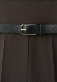 Ceinture en cuir noir avec boucle rectangulaire en or attachée autour d'un tissu plissé marron foncé.