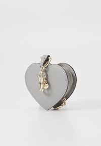 Portafoglio a forma di cuore grigio chiaro in pelle, con zip e minuteria dorata, dotato di un anello portachiavi sul lato.