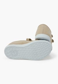 Baskets en toile beige avec une semelle en caoutchouc bleu clair et un relief texturé. Dispose d'une sangle à boucle pour le maintien. Design minimaliste sans embellissements.