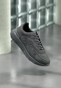 Zapato deportivo gris con un dise�ño curvo y superficie texturizada, con cordones y una suela estampada para mayor tracción.